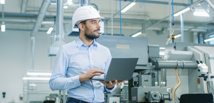 Man stands with laptop in production hall and checks the processes (c) Shutterstock / Gorodenkoff