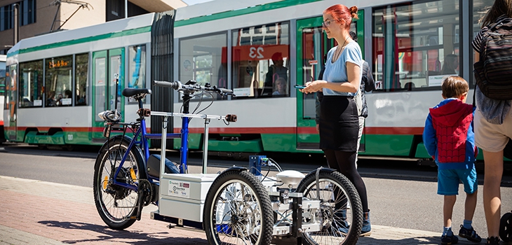 Woman stands with autonomous cargo bike in front of a train stop (c) Jana Dünnhaupt Uni Magdeburg