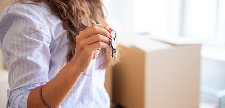 A woman is holding a key in her hand. Moving boxes can be seen in the background. (Photo: magnific)