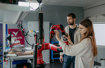 Isabell Meißner und Erik Hanau im Humtech Lab mit einem Roboterarm (c) Jana Dünnhaupt Uni Magdeburg