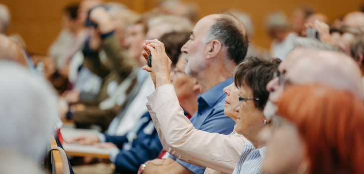 Momente des Erinnerns – das Publikum lauscht und hält fest Zuschauerinnen und Zuschauer sitzen in einem Hörsaal und folgen aufmerksam einer Veranstaltung. Eine Person hält ein Smartphone hoch und macht offenbar ein Foto oder Video ©Jana Dünnhaupt, Uni Magdeburg
